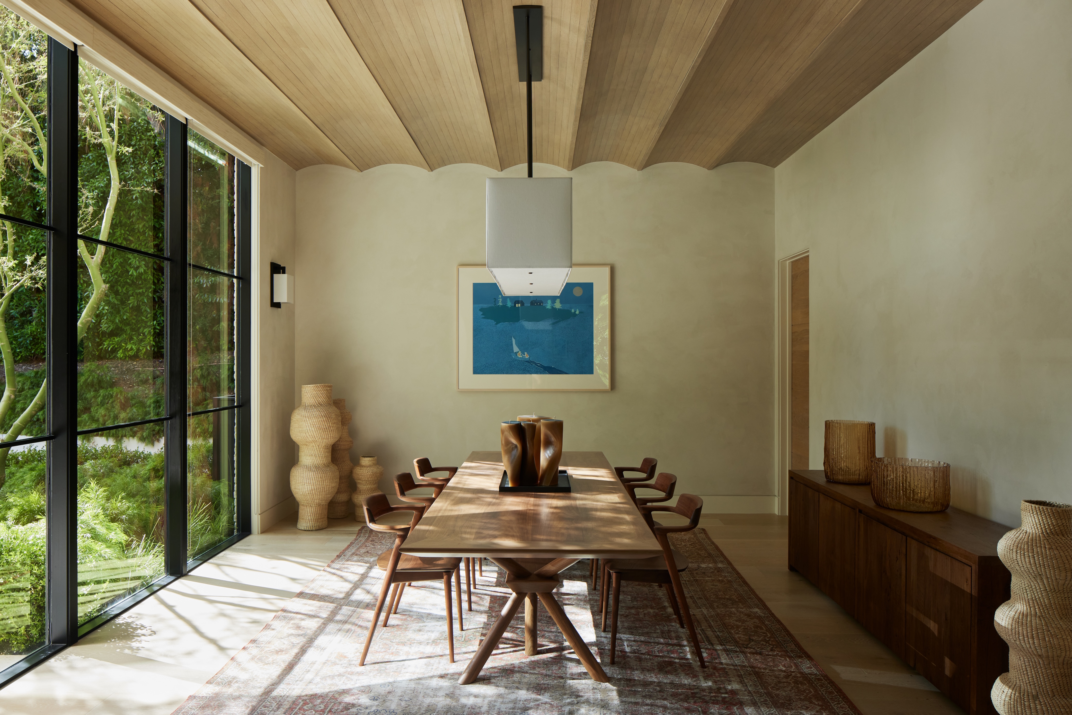 Sunlit dining room designed by Reddymade with large wall of windows and wooden table and chairs